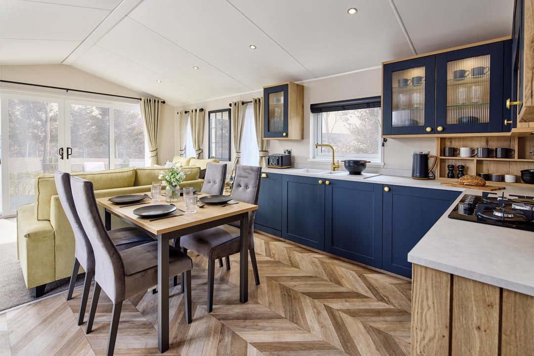 016_sf_whh_gainsborough_lodge_c5f657c672 This is a huge Open Plan lounge kitchen, with a four seater table and chairs, white double sink with gold taps light worktops, blue cupboard doors and a huge four paned patio sliding doors.