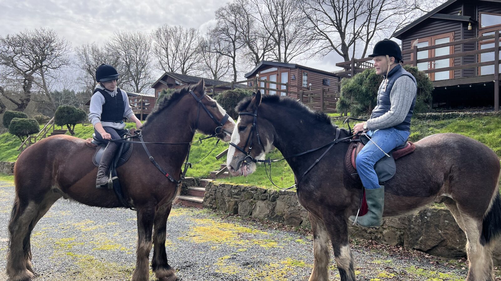 Two riders on horseback, one old, one young outside the lodges at Bank Farm Holiday Park.