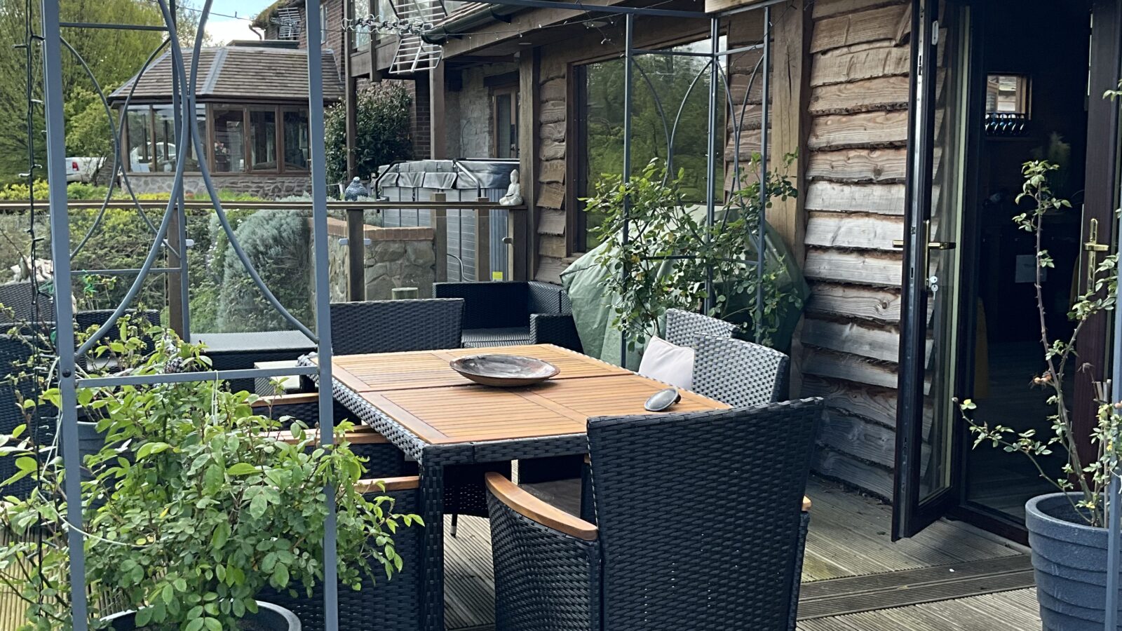 Outside the spa lodge on the huge decking balcony with plants, canopy, table and chairs ...